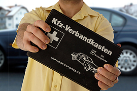 Ein Mann hält einen schwarzen Kfz-Verbandkasten in den Händen