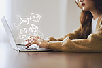 Frau nutzt Laptop und versendet Online-Nachrichten mit E-Mail-Symbol