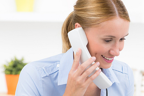 Eine freundliche junge Damen hält einen Telefonhörer in der Hand
