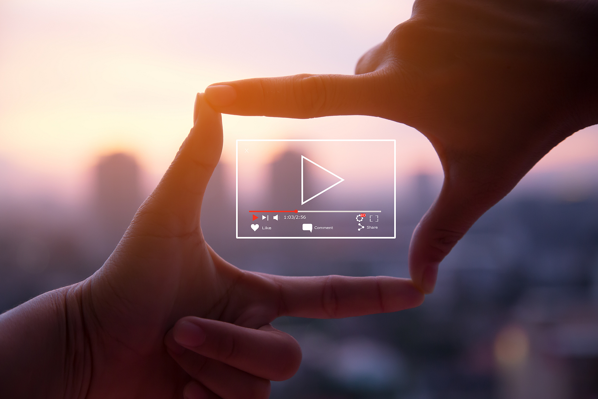 Person formt mit den Fingern vor rosafarbenem Himmel ein Quadrat in dem ein Video läuft.